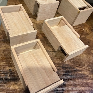 Puede incluir: Cinco cajas de madera con tapas, todas abiertas y dispuestas sobre una superficie de madera. Las cajas son de madera clara y tienen un diseño simple y minimalista.