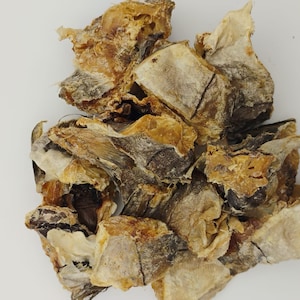 May include: A pile of dried fish pieces, with a light brown and white color, on a white surface.
