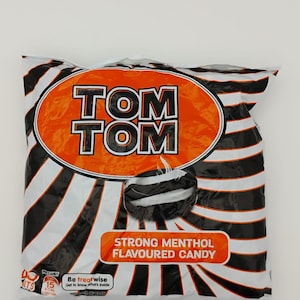 May include: A bag of Tom Tom Strong Menthol Flavoured Candy. The bag is black and white with orange text and a picture of a black and white candy.