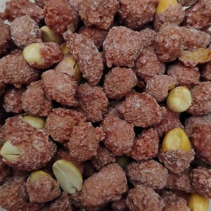 May include: A close-up of a bowl filled with red-colored peanuts covered in a white, sugary coating.