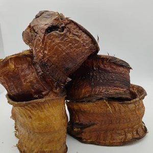 May include: A stack of four dried, smoked fish, with a brown and golden color. The fish are curled into a circular shape, with the skin visible.