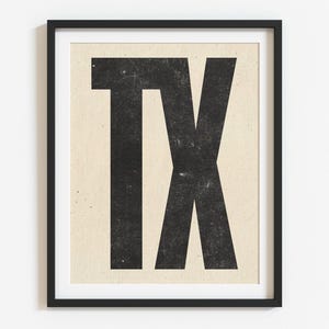 May include: Framed art print featuring the letters "TX" in a bold, distressed black font against a beige background. The artwork is encased in a black frame, suitable for wall decor.