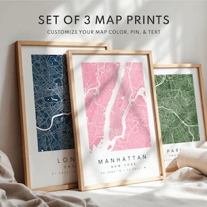 May include: Set of three framed map prints. The maps feature city layouts in navy blue, pink, and green, with the names of the cities printed below. The text "SET OF 3 MAP PRINTS" and "CUSTOMIZE YOUR MAP COLOR, PIN, & TEXT" are at the top.