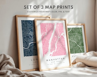 May include: Set of three framed map prints. The maps feature city layouts in navy blue, pink, and green, with the names of the cities printed below. The text "SET OF 3 MAP PRINTS" and "CUSTOMIZE YOUR MAP COLOR, PIN, & TEXT" are at the top.
