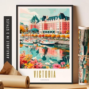 May include: A framed art print of Victoria, Canada, featuring a pink building with a dark roof, boats on the water, and colorful flowers. The print is in a black frame, with the words "VICTORIA CANADA" at the bottom. The words "AVAILABLE IN 3 STYLES" are on the side.