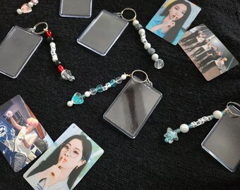 May include: A collection of clear plastic keychains with colorful beaded charms. The charms spell out the words "TWICE", "BP", and "NZK".