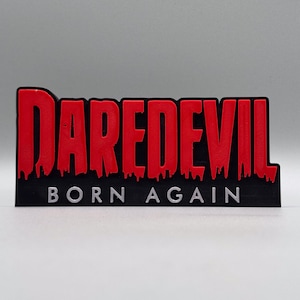 Peut inclure: Une enseigne en 3D imprimée en noir et rouge avec les mots "Daredevil Born Again" en lettres blanches.