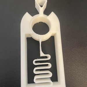 以下が含まれることがあります： ユニークなデザインの白い3Dプリントオブジェクト。円形の開口部、長方形のフレーム、内部の波状の蛇のような形が特徴です。上部には幾何学的な形状があり、全体的な形状は抽象的でモダンです。