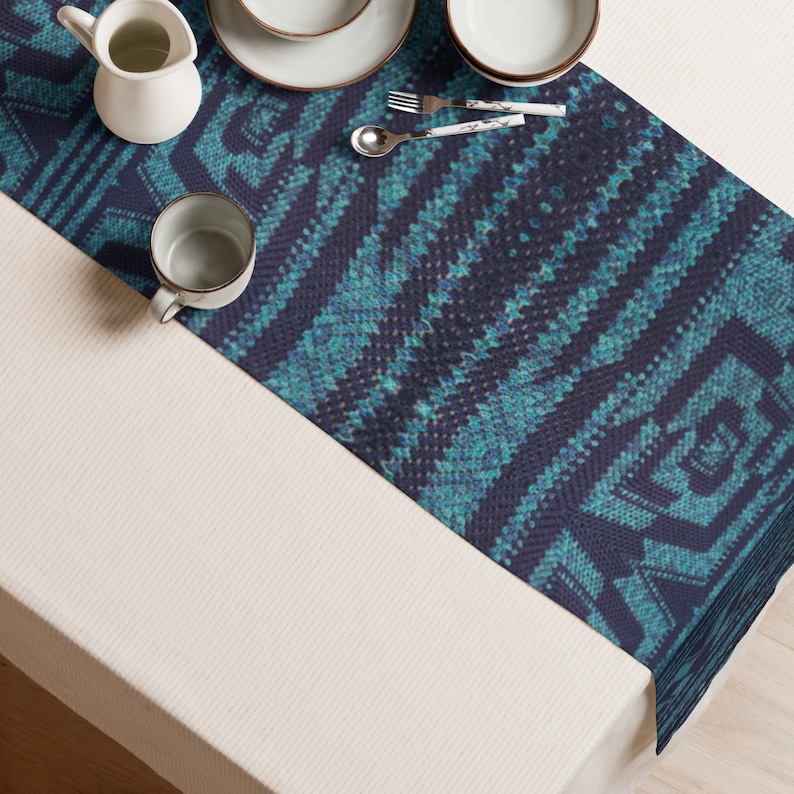 Puede incluir: Un camino de mesa con estampado azul marino y turquesa con un dise&ntilde;o geom&eacute;trico. El camino de mesa est&aacute; colocado sobre un mantel blanco y est&aacute; rodeado de vajilla blanca, una jarrita de crema y una taza. Tambi&eacute;n se ve cuberter&iacute;a con mangos estampados en blanco y gris.