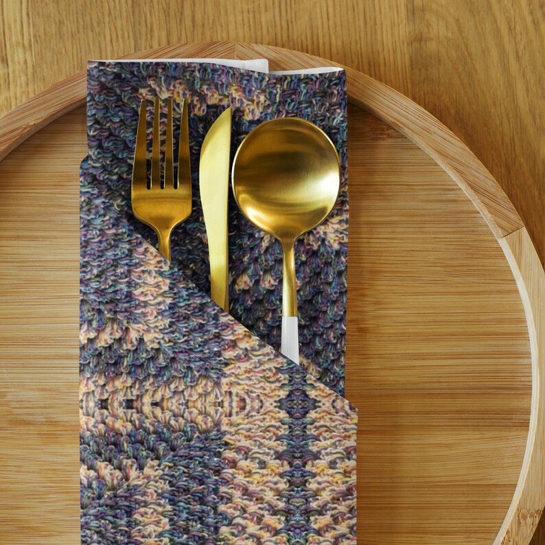 Puede incluir: Un juego de tenedor, cuchillo y cuchara dorados sobre una servilleta estampada. La servilleta est&aacute; doblada y colocada sobre una bandeja de bamb&uacute;. La cuberter&iacute;a tiene un dise&ntilde;o moderno.