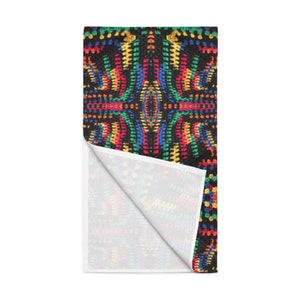 May include: A black and white towel with a colorful, geometric pattern. The design features a repeating pattern of red, yellow, blue, and green dots. The towel is folded over, revealing a white underside.