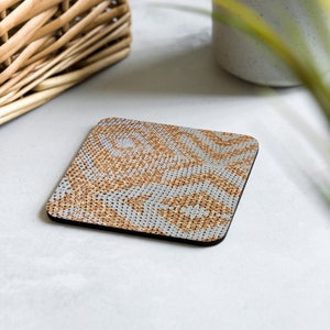 May include: Square coaster featuring a repeating pattern in tan and grey. The coaster has a black border and is likely made of a durable material. The design gives the coaster a textured appearance, suitable for home decor.