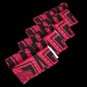 May include: Rolled fabric with a geometric pattern in pink and orange hues on a black backdrop. The design features repeating squares and angular shapes, giving a textured look. The fabric is likely for home decor, with measurements in centimetres.