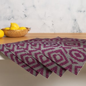 Pode incluir: Quatro individuais com um padr&atilde;o geom&eacute;trico em tons de cinza e magenta est&atilde;o dispostos sobre uma superf&iacute;cie de madeira. Uma cesta de vime cheia de lim&otilde;es est&aacute; no fundo. Os individuais t&ecirc;m uma apar&ecirc;ncia texturizada.