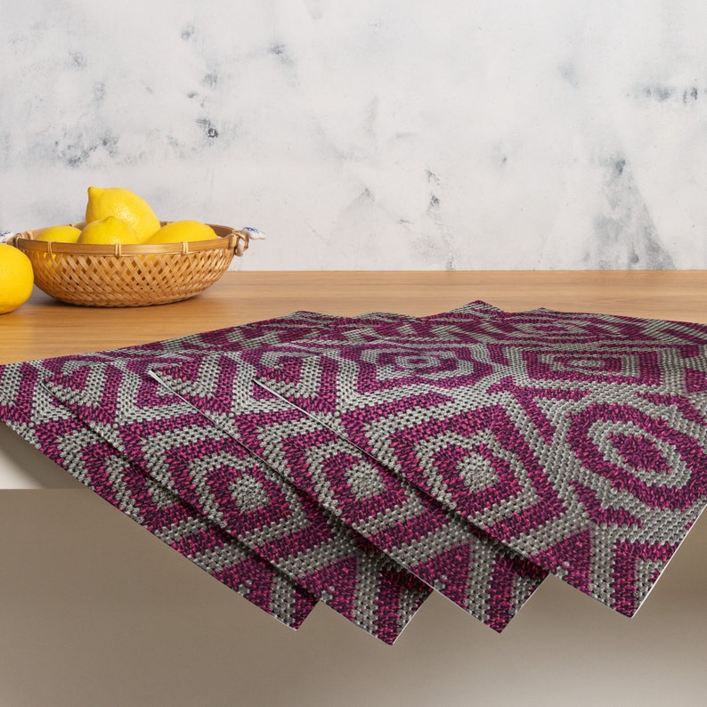 Pode incluir: Quatro individuais com um padr&atilde;o geom&eacute;trico em tons de cinza e magenta est&atilde;o dispostos sobre uma superf&iacute;cie de madeira. Uma cesta de vime cheia de lim&otilde;es est&aacute; no fundo. Os individuais t&ecirc;m uma apar&ecirc;ncia texturizada.