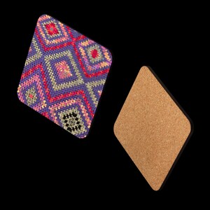 以下が含まれることがあります： 2つのひし形のコースター。1つは、紫、ピンク、赤、黄色の色合いのカラフルな幾何学模様の編み物です。もう1つのコースターはコルク製です。