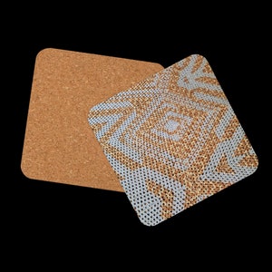 May include: Two square coasters. One is plain cork, the other has a geometric pattern in light blue and gold. The patterned coaster is on top of the cork coaster, with a black background.