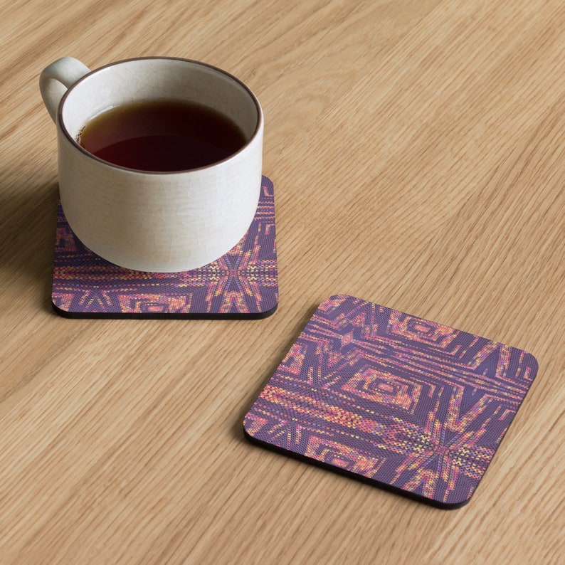 May include: Two square coasters with a geometric design in purple, orange, and yellow. One coaster supports a white mug filled with tea. The coasters are on a light wood surface. The design features a starburst pattern.