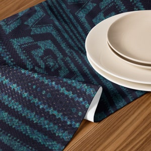Puede incluir: Un camino de mesa con estampado azul marino y verde azulado con un dise&ntilde;o geom&eacute;trico. Dos platos blancos est&aacute;n apilados en el lado derecho del camino de mesa. El camino de mesa est&aacute; hecho de tela texturizada.