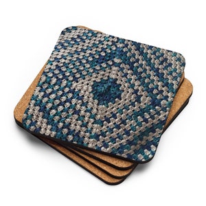 Op de afbeelding: Een stapel van vier vierkante onderzetters. De bovenste onderzetter heeft een gedetailleerd haakpatroon in blauw, teal en cr&egrave;me. Het patroon is een herhalend vierkant. De onderzetters zijn ongeveer 10 cm x 10 cm groot.