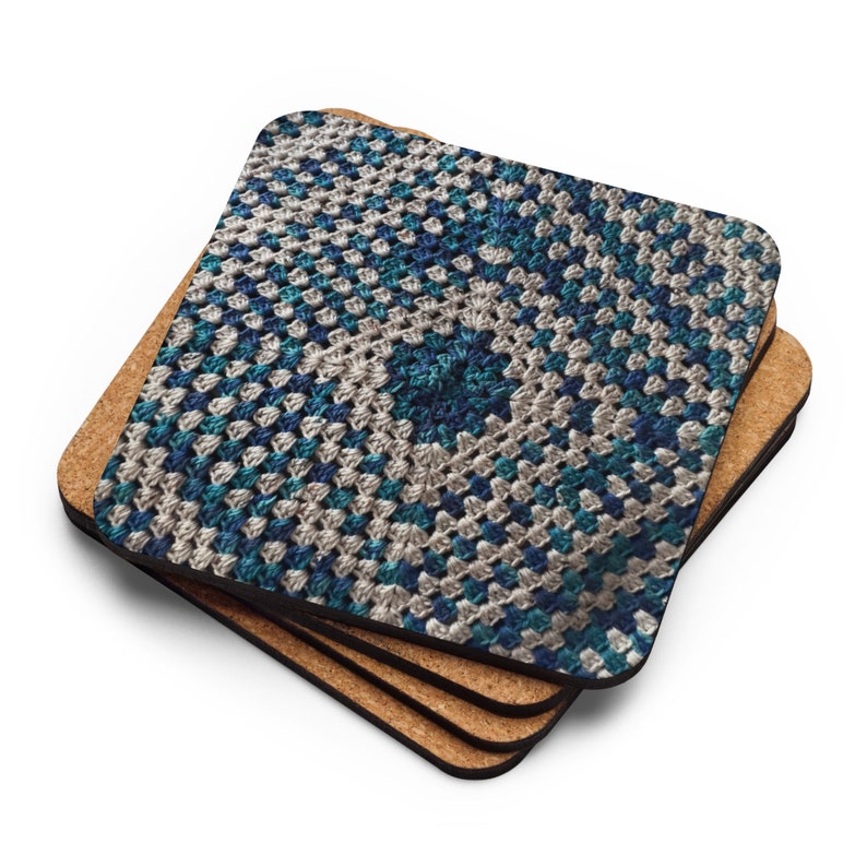 Op de afbeelding: Een stapel van vier vierkante onderzetters. De bovenste onderzetter heeft een gedetailleerd haakpatroon in blauw, teal en cr&egrave;me. Het patroon is een herhalend vierkant. De onderzetters zijn ongeveer 10 cm x 10 cm groot.