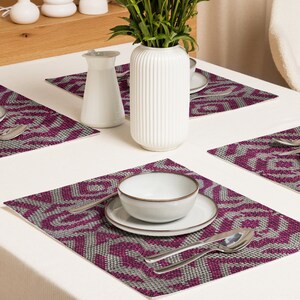 Pode incluir: Uma mesa de jantar com quatro individuais. Cada individual tem um padr&atilde;o geom&eacute;trico em tons de cinza e magenta. Um vaso branco com caules verdes, um cremeira e uma tigela com um prato est&atilde;o sobre a mesa. Os talheres est&atilde;o colocados nos individuais.
