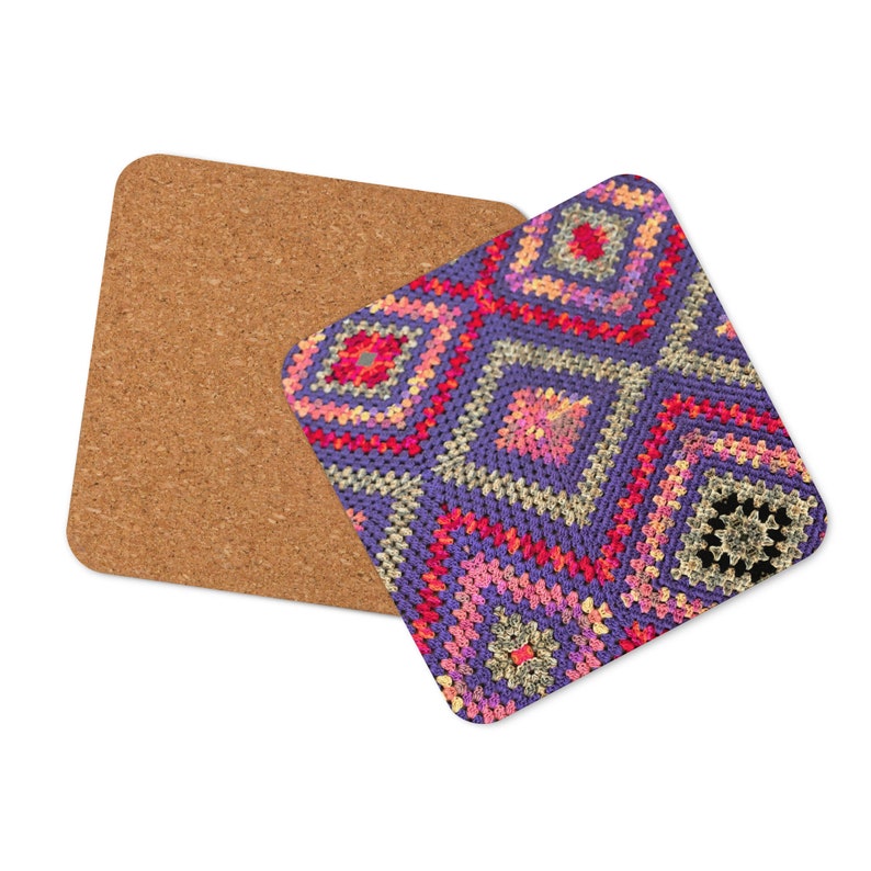 May include: Square coaster with a cork backing and a colorful, geometric crochet design. The crochet pattern features a repeating diamond motif in shades of purple, pink, red, and yellow. The coaster is designed to protect surfaces from drink rings.