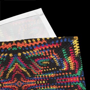 Op de afbeelding: Close-up van een zwart textiel met een levendig, geometrisch patroon. Het ontwerp bevat een verscheidenheid aan kleuren, waaronder rood, oranje, geel, groen en blauw. De bovenrand van het textiel is wit.