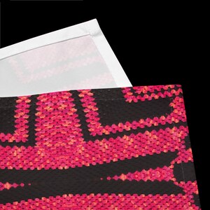 May include: Close-up of a black textile with a vibrant pink and orange floral pattern. The design features a repeating geometric motif. A white fabric edge is visible in the upper corner, suggesting a larger piece of fabric.
