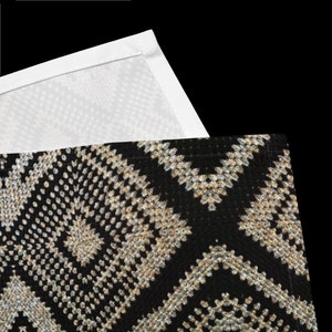 May include: A black and beige patterned textile with a geometric design. The pattern features diamond and zig-zag shapes. A white textile with a dotted pattern is visible in the upper portion of the image.