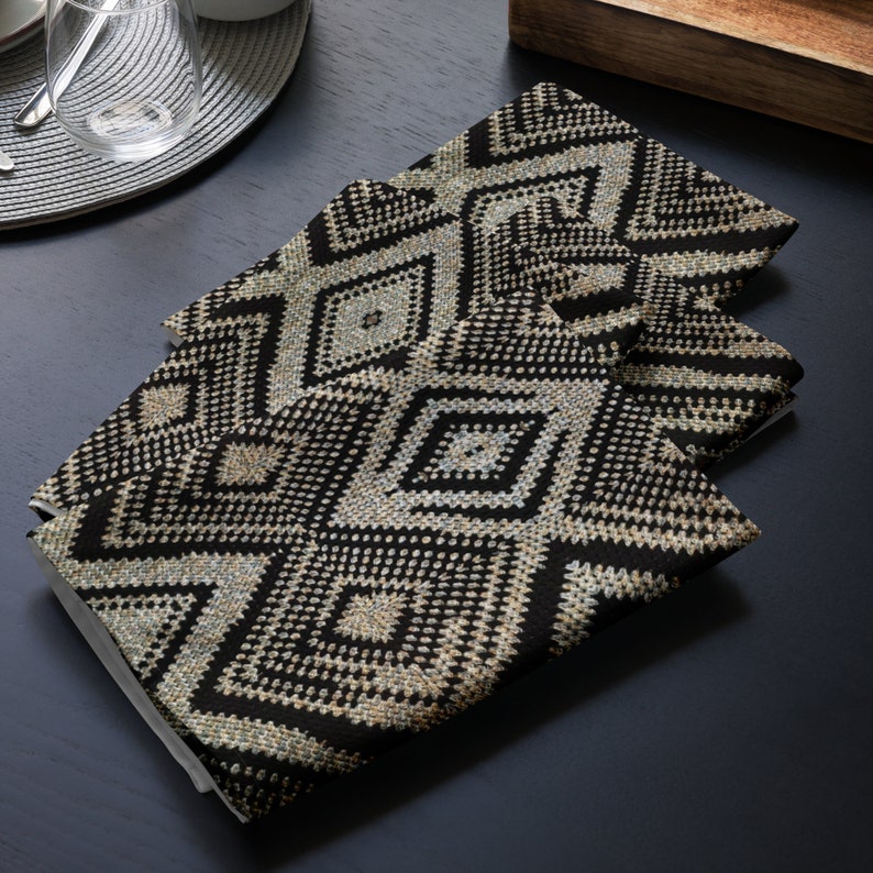 May include: Four folded black and beige geometric patterned cloth napkins. The napkins feature a repeating diamond design. The napkins are made of a textured fabric and are stacked on top of each other. The napkins are on a dark surface.