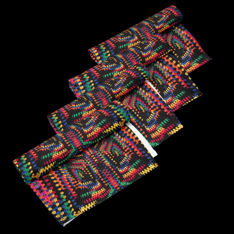 Op de afbeelding: Zwarte stof met een kleurrijk, geometrisch patroon in rood, geel, groen en blauw. De stof is opgerold en gevouwen, waardoor het ontwerp wordt getoond. Het patroon lijkt op een haak- of breistijl.