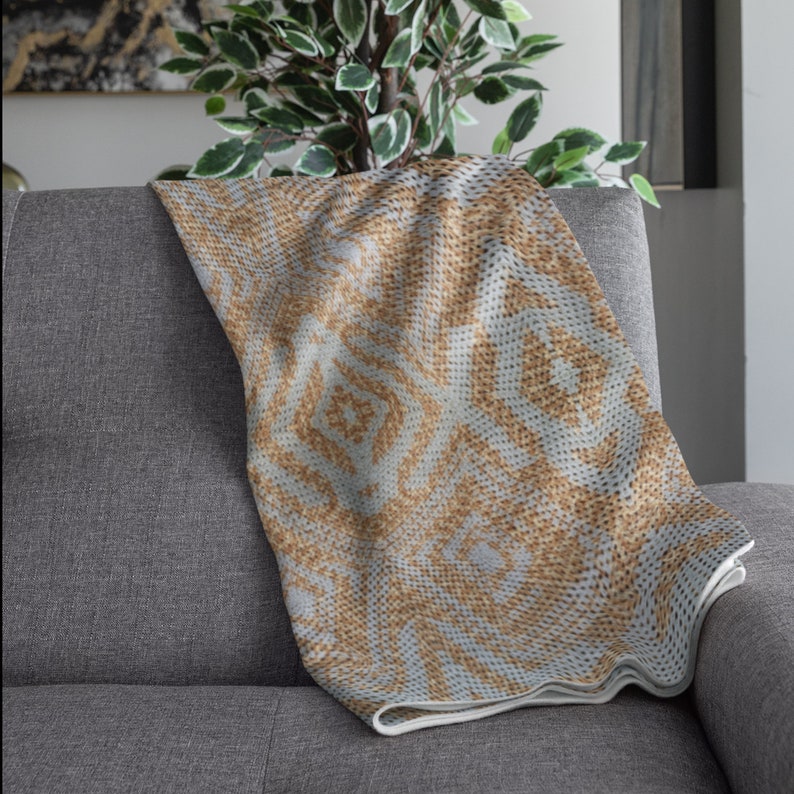 Pode incluir: Uma manta dobrada com um padr&atilde;o geom&eacute;trico em tons de bege e cinza claro repousa sobre um sof&aacute; cinza. O design da manta apresenta formas de diamante e espiral. As bordas s&atilde;o finalizadas com uma borda branca, adicionando um contraste limpo.