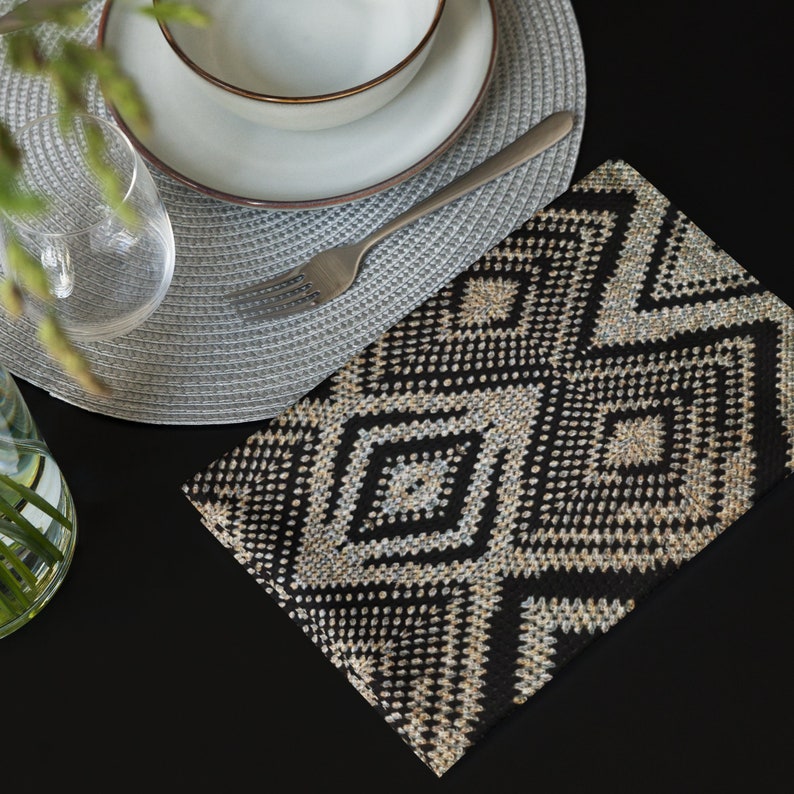 May include: A black and beige geometric patterned placemat is placed on a black surface. A gray woven placemat, a white bowl with a brown rim, a fork, and a clear glass are also visible. The scene suggests a dining setting.