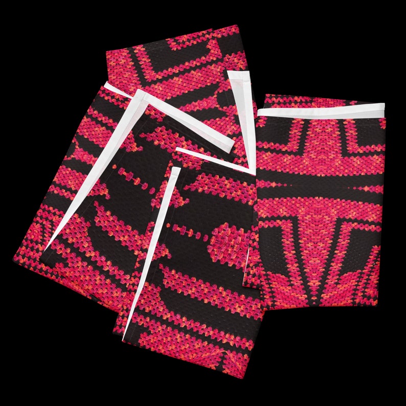 May include: Several folded black fabric items with a vibrant pink and orange geometric pattern. The pattern features a repeating design of angular shapes and lines. The edges of the fabric are white.
