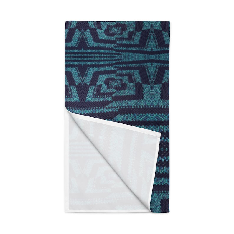 Puede incluir: Un textil rectangular con estampado en azul turquesa y azul marino con una esquina doblada, que revela un interior blanco. El dise&ntilde;o presenta formas geom&eacute;tricas y l&iacute;neas, creando una apariencia texturizada. El textil es probablemente una toalla o una manta.