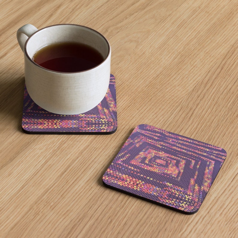 May include: A white ceramic mug filled with tea rests on a square coaster featuring a geometric design in purple, pink, and yellow hues. A second coaster with the same pattern is visible. The coasters are on a light wood surface.