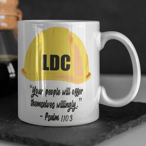 May include: White ceramic mug with a yellow hard hat with the letters "LDC" on it. The mug has the quote "Your people will offer themselves willingly." - Psalm 110:3 printed on it.