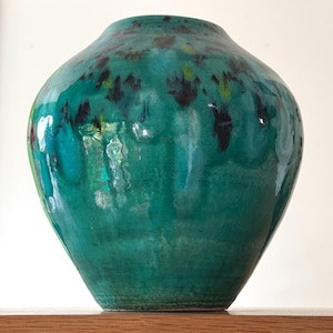 May include: A large, round, green ceramic vase with a glossy finish. The vase has a mottled pattern of black and green.