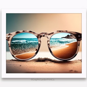 Puede incluir: Un par de gafas de sol de carey marrón con una escena de playa reflejada en las lentes. Las gafas de sol están tumbadas en una playa de arena.