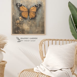 Puede incluir: Una impresi&oacute;n enmarcada de una mariposa con alas naranjas y marcas negras sobre un fondo azul claro texturizado. La impresi&oacute;n est&aacute; en un marco de madera y est&aacute; colgada en una pared blanca.