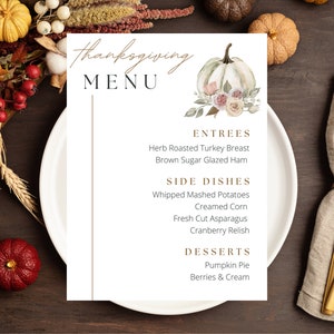 May include: A Thanksgiving menu with a watercolor illustration of a white pumpkin with pink flowers. The menu lists entrees, side dishes, and desserts. The entrees are Herb Roasted Turkey Breast and Brown Sugar Glazed Ham. The side dishes are Whipped Mashed Potatoes, Creamed Corn, Fresh Cut Asparagus, and Cranberry Relish. The desserts are Pumpkin Pie and Berries & Cream.