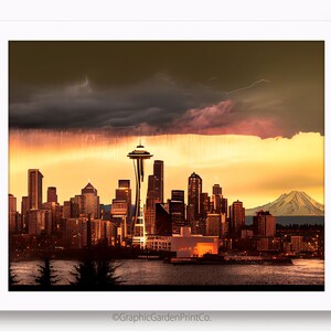 May include: A panoramic view of the Seattle skyline at sunset, with the Space Needle in the foreground and Mount Rainier in the background. The sky is a mix of dark clouds and a bright orange sunset.