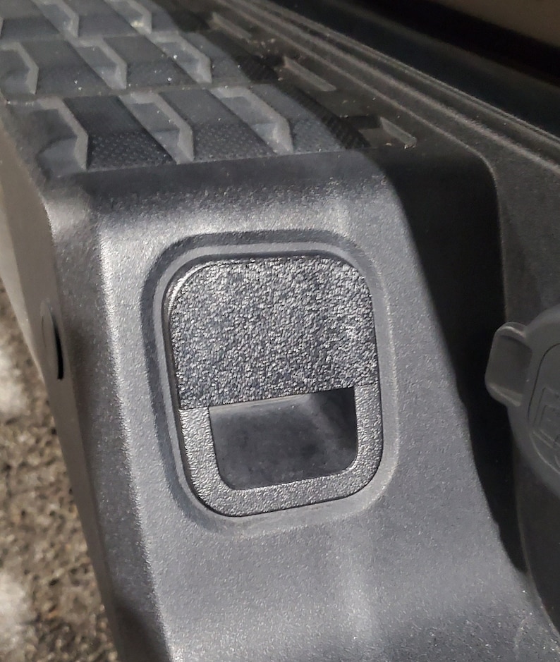 Może przedstawiać: Zbliżenie na czarny plastikowy panel dostępowy w pojeździe. Panel ma teksturę i prostokątny otw&oacute;r.