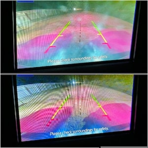 Op de afbeelding: Een achteruitkijkcamera-display met een roze en blauwe achtergrond met gele en groene lijnen. De tekst "Controleer de omgeving voor de veiligheid." wordt onderaan het scherm weergegeven.