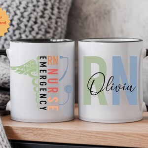 May include: White ceramic mug with a black handle and rim. One side features the words "RN Nurse Emergency" with a caduceus and stethoscope graphic. The other side displays "RN" and the name "Olivia".