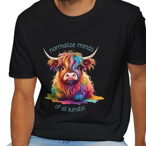Puede incluir: Una camiseta negra con una ilustración colorida de una vaca Highland y el texto "normalizar las mentes de todo tipo!"