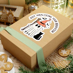 May include: A white ghost wearing a witch hat and holding a broom with a black cat sitting below. The text around the ghost says "Just analyzing your behavior".