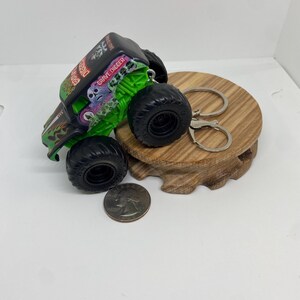 以下が含まれることがあります： 黒と緑の Grave Digger モンスター トラック キーホルダー。大きな黒いタイヤが付いています。キーホルダーにはシルバーのリングと留め金が付いています。サイズの比較のために、トラックの横にコインがあります。トラックには「Grave Digger」の文字があります。