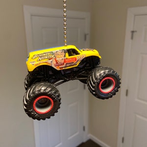 May include: A yellow monster truck toy with black wheels and red rims. The truck has a blue and white design on the side with the words "Bounty Hunter" and "Hedman Headers 60 Years".